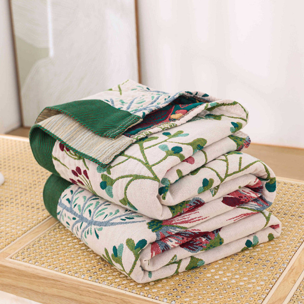 A neatly folded stack of vintage botanical floral cotton throw blankets resting on a rattan bench.