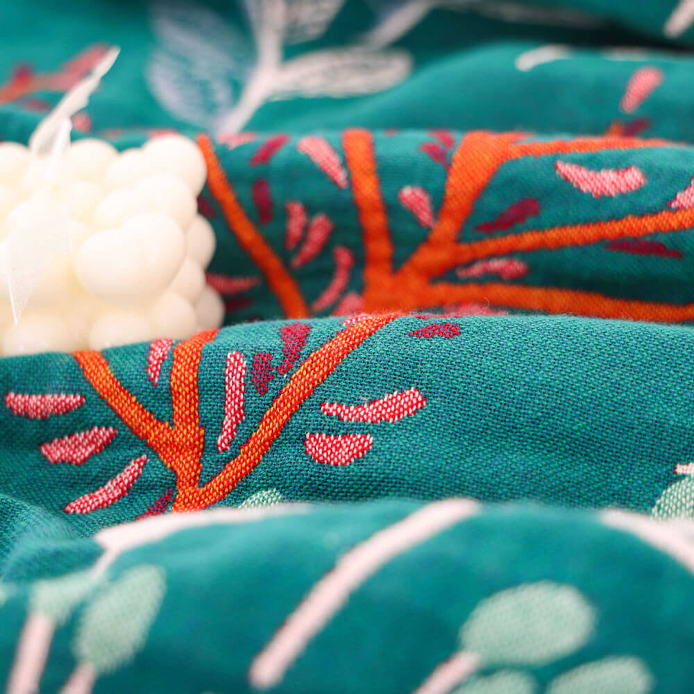 Macro detail of the woven cotton fabric of a teal floral throw blanket, highlighting the high-quality texture and orange branch pattern.