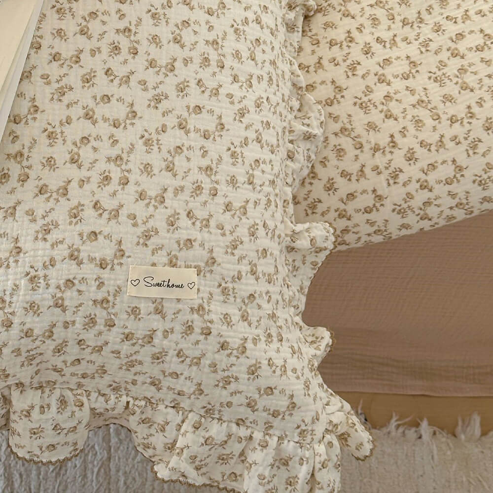 An overhead shot of a vintage camellia cotton gauze duvet cover set on a bed, showcasing the delicate floral print and the ruffled edges with contrasting stitching. The bedding is styled with a solid khaki flat sheet and matching pillows, creating a rustic and cozy bedroom aesthetic.