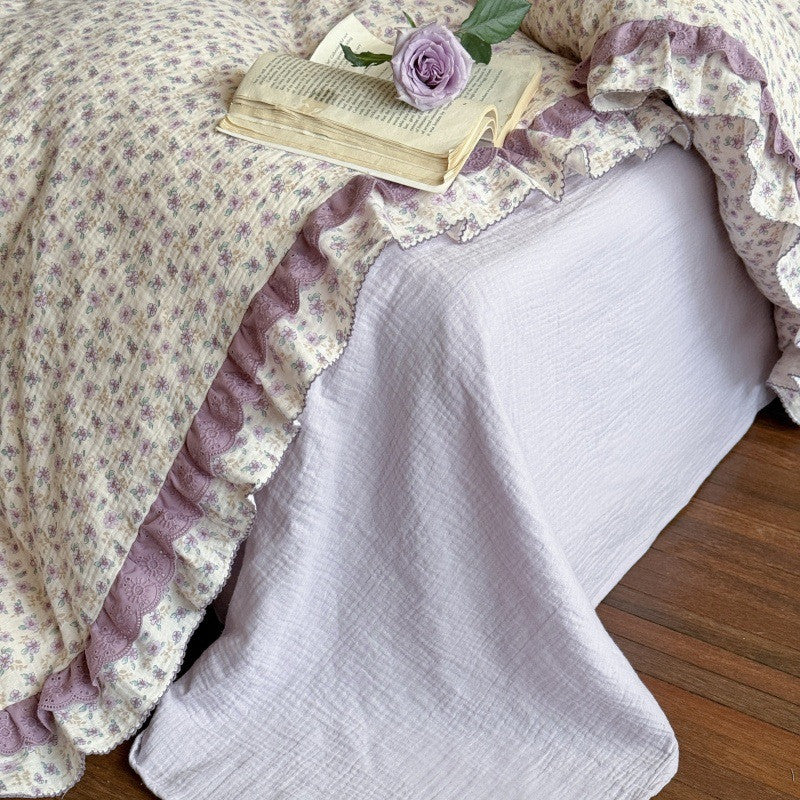 Close-up of the mattress corner showing the solid light purple/lavender fitted sheet paired with the ruffled lace edge of the floral duvet cover.