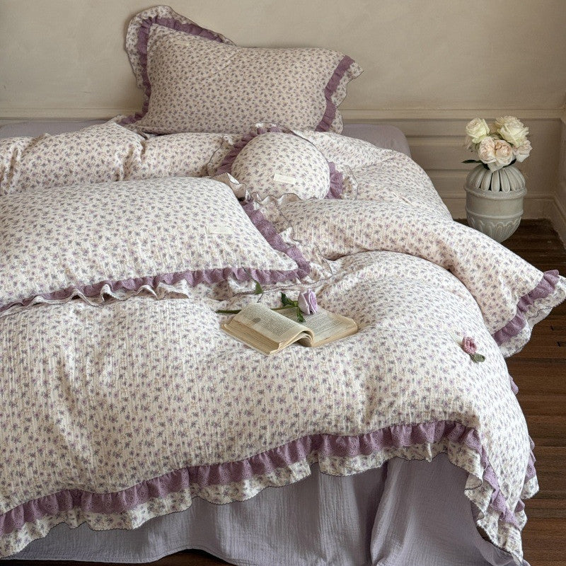 Full view of the romantic cottage style bedding set, highlighting the lavender-purple fitted sheet underneath and the layered ruffled floral pillowcases.