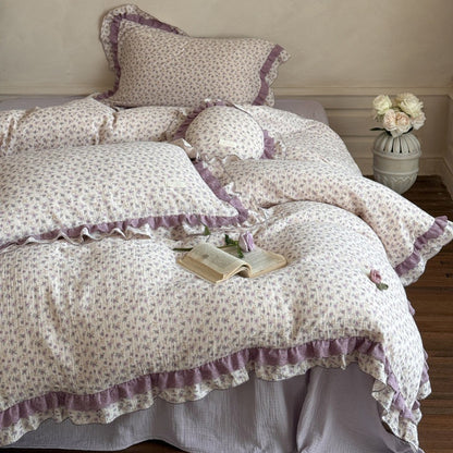 Full view of the romantic cottage style bedding set, highlighting the lavender-purple fitted sheet underneath and the layered ruffled floral pillowcases.