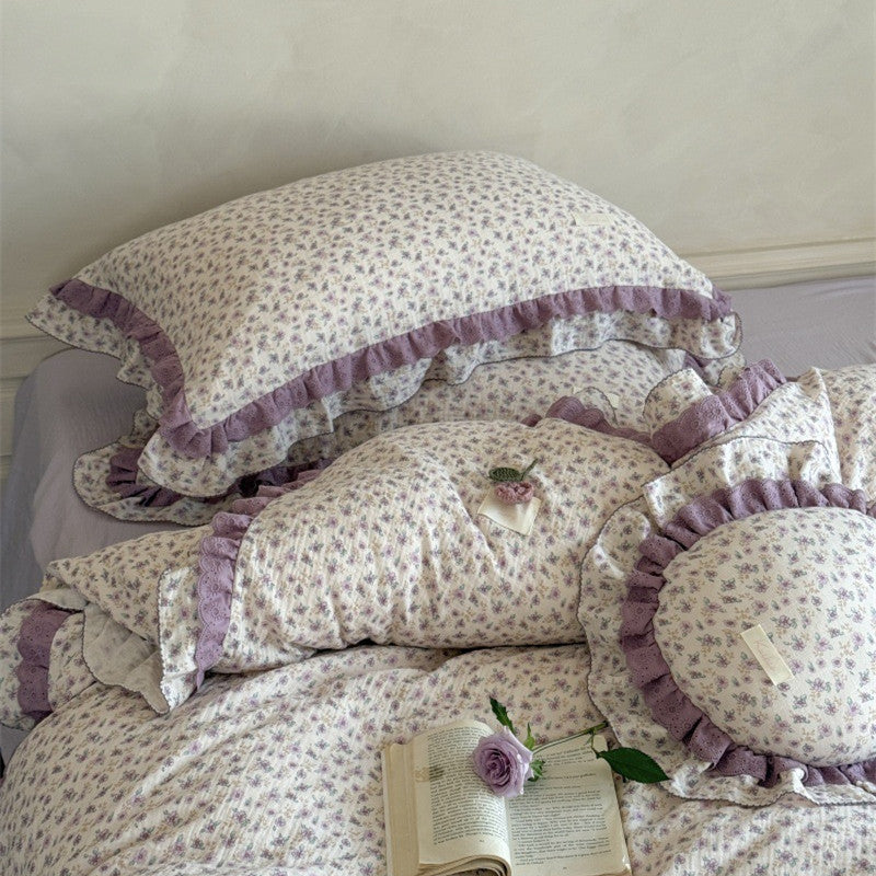 Close-up of the textured crinkle cotton pillow shams with elegant purple eyelet lace ruffles, paired with an open vintage book and a fresh purple rose.