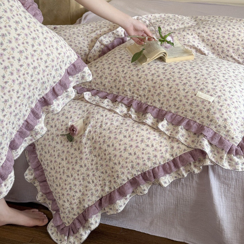 A close-up shot showing someone arranging the purple floral lace bedding, displaying the soft breathable fabric texture and detailed scalloped lace edges.