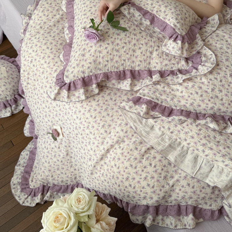 An overhead view of the purple floral lace duvet cover, showcasing the matching round throw pillow and a hand holding a lavender rose for a romantic aesthetic.