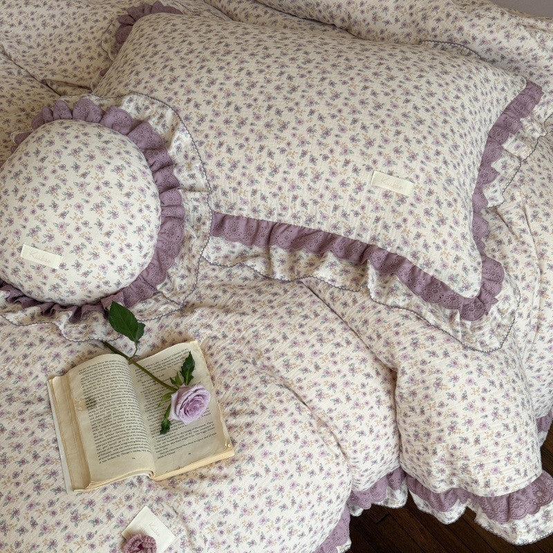 Macro detail of the purple ditsy floral bedding fabric, featuring the unique 'kuibao' brand label stitched onto the ruffled lace pillow sham.