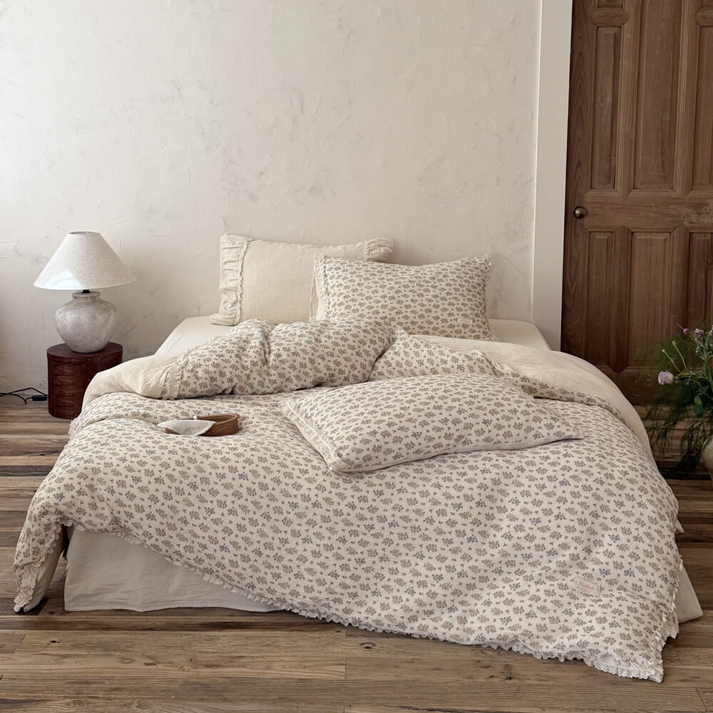 Detailed close-up of a cream-colored plain bed skirt under a draped vintage floral summer comforter with eyelet lace trim.