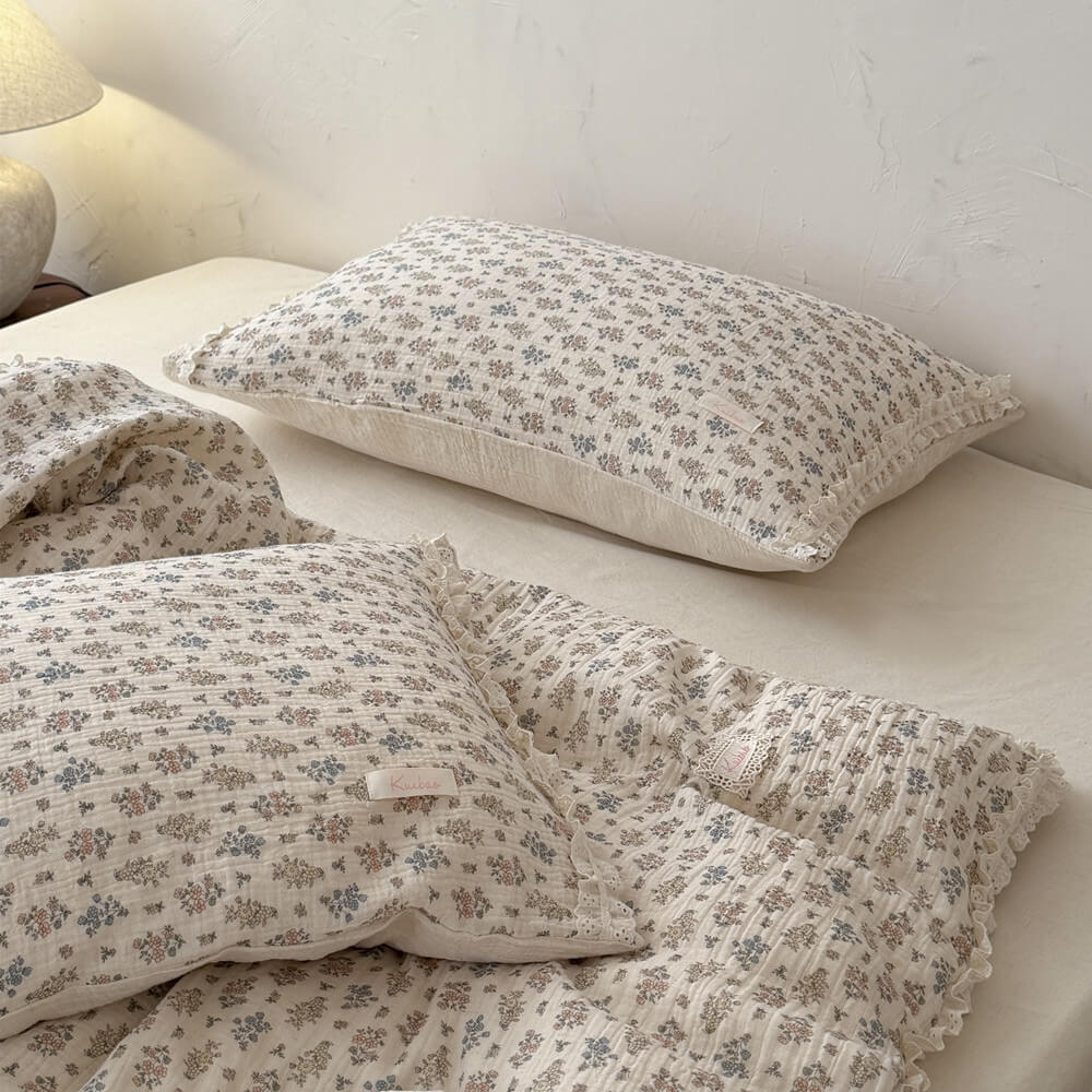 Close-up of a soft, crinkled cotton vintage floral summer comforter with detailed eyelet lace trim draped over a bed.
