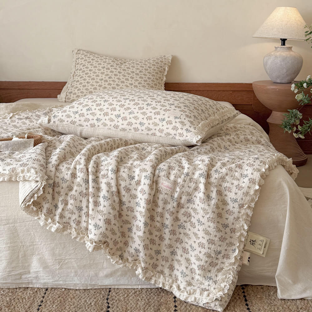 Vintage floral summer comforter with delicate lace ruffle trim casually draped over a bed with matching ditsy flower pillows.