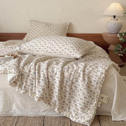 Vintage floral summer comforter with delicate lace ruffle trim casually draped over a bed with matching ditsy flower pillows.