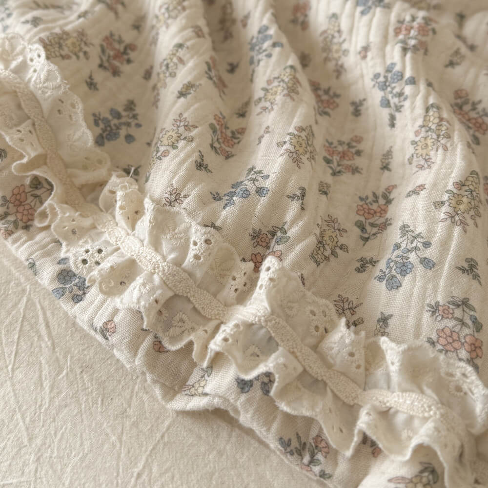 Macro texture shot of the breathable, textured linen-cotton fabric on a vintage floral summer blanket highlighting the eyelet lace ruffle.