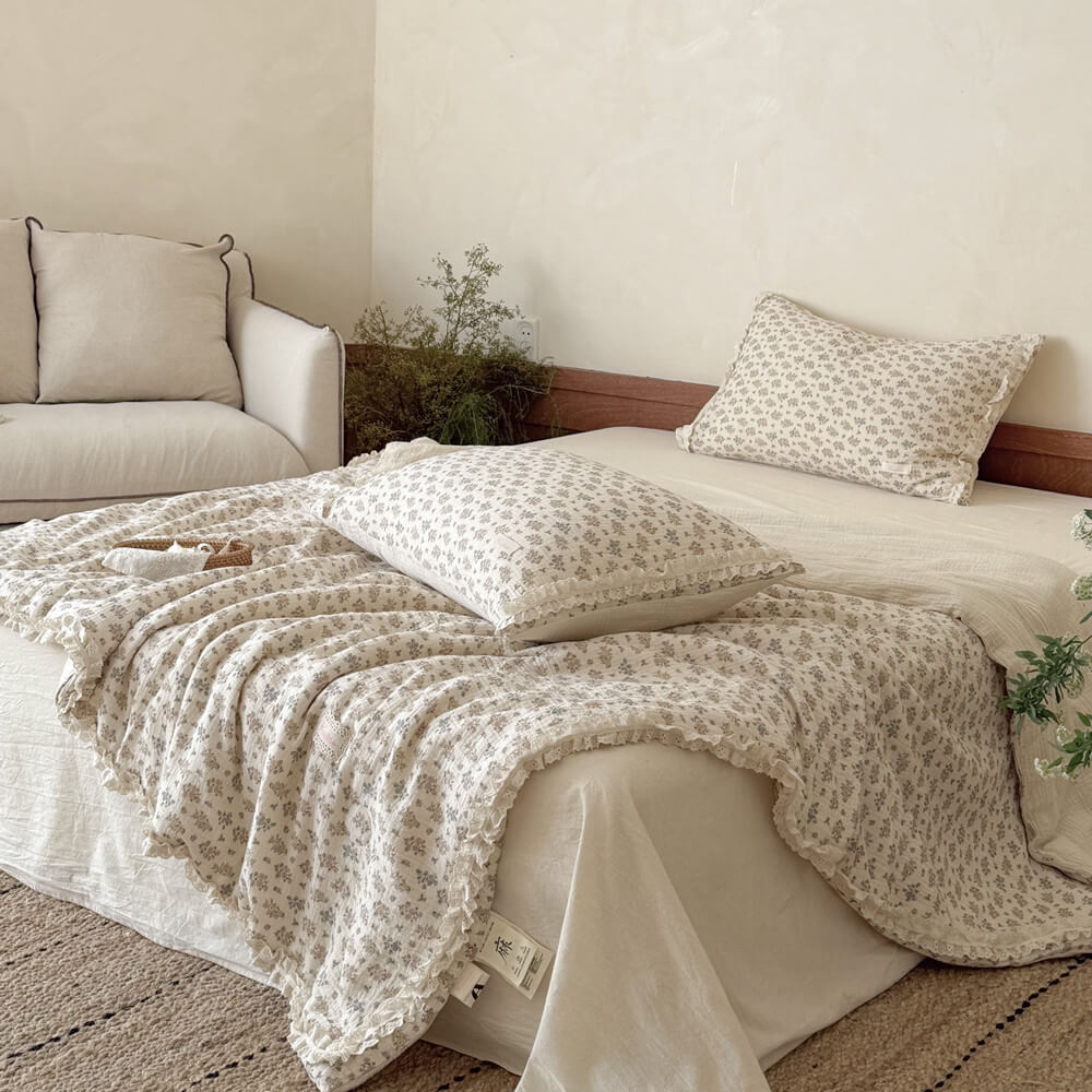 Wide shot of a cozy cottagecore bedroom featuring a lightweight vintage floral summer quilt on a bed next to a white sofa.