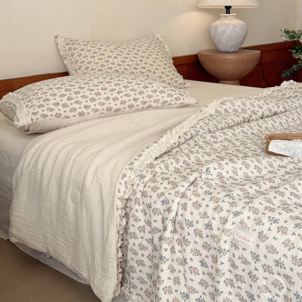Side view of a reversible vintage floral summer blanket flipped over to show its solid cream-colored underside and ruffled lace edges.
