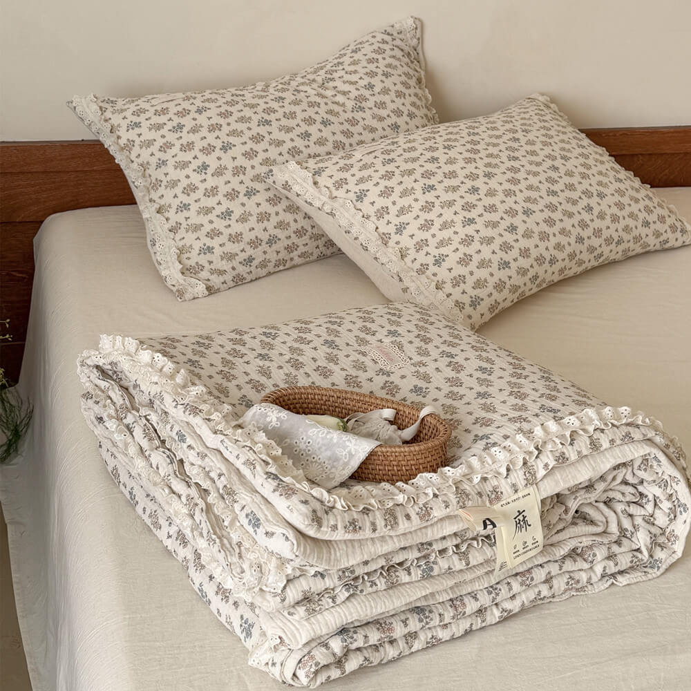 Neatly folded vintage floral summer comforter with intricate ruffled lace edges stacked neatly on a beige sheet.