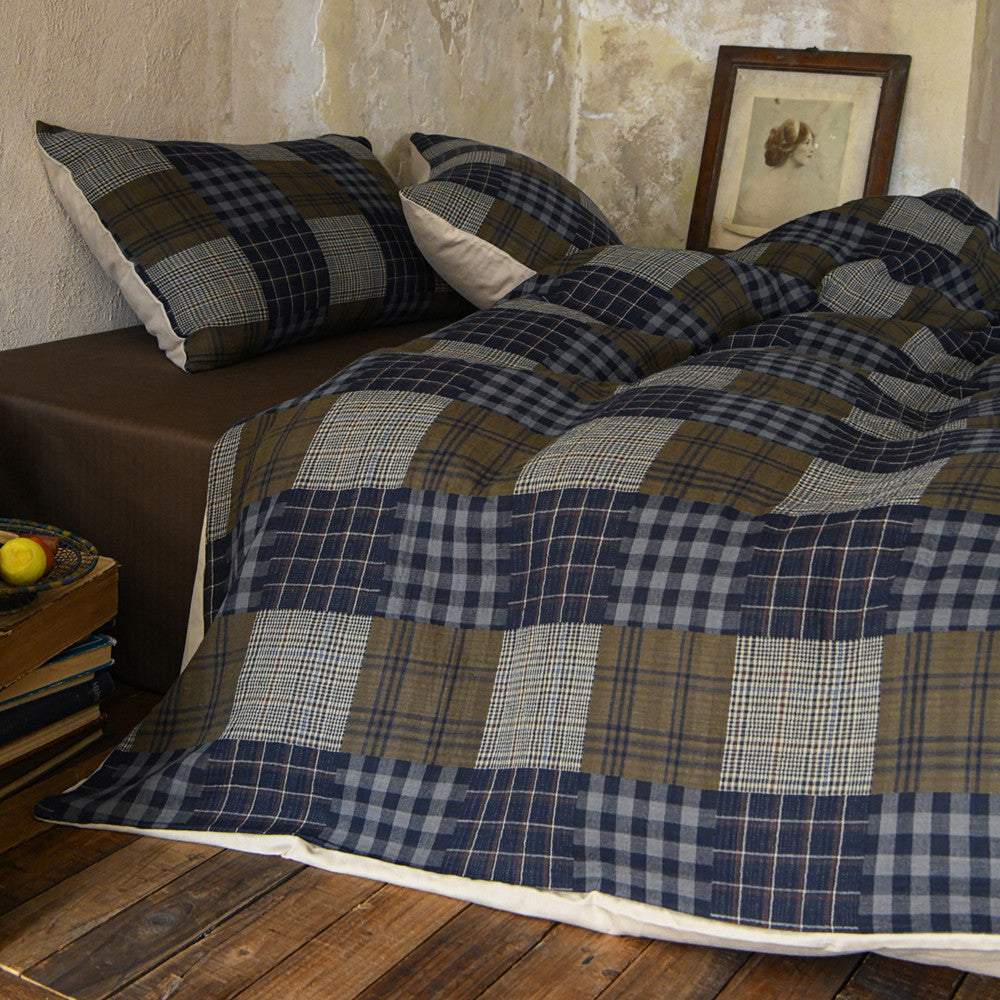 Plaid blanket and pillows on a bed in a rustic bedroom setting.