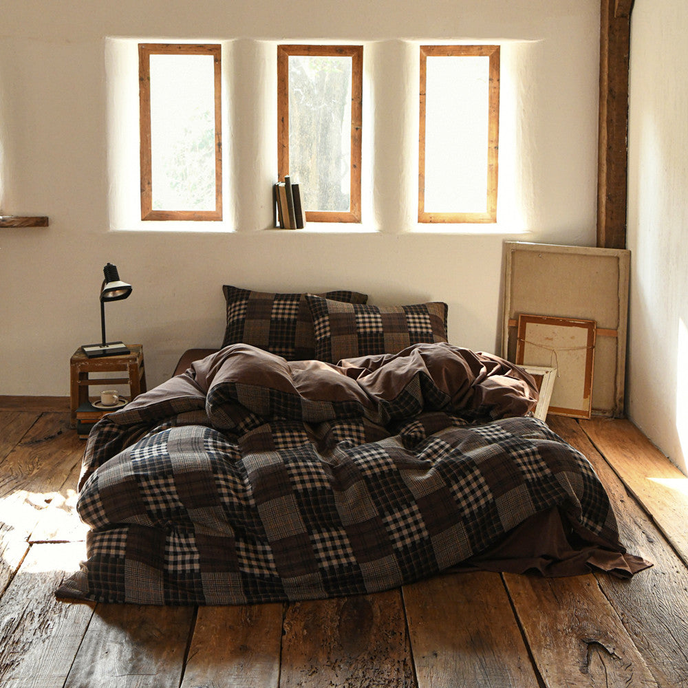 Plaid bedding set on a bed in a room with wooden floors and large windows.
