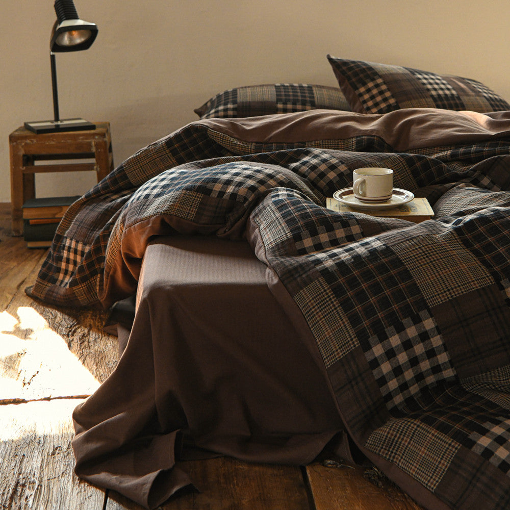 Bed with plaid bedding and a cup on a wooden nightstand.