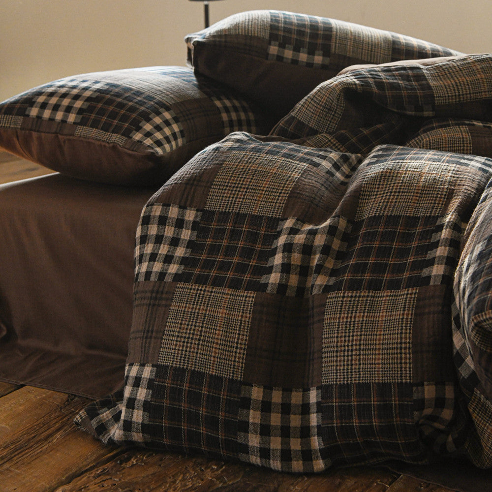 Plaid duvet cover and pillows on a bed with a wooden floor and beige wall in the background