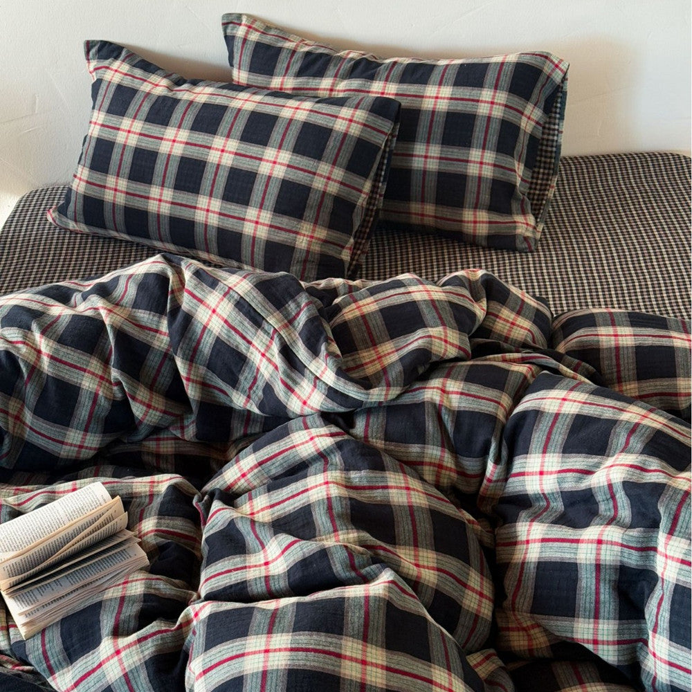 Close-up of the vintage plaid pattern on a cotton muslin duvet and two pillows, highlighting the breathable, soft texture of the crinkled fabric.