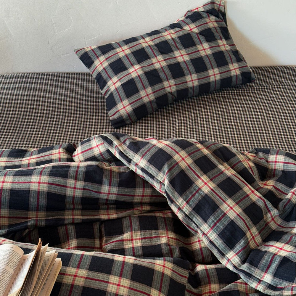 Detail view of the cotton muslin duvet cover set showing the contrast between the large dark plaid duvet and the small gingham-style fitted sheet.