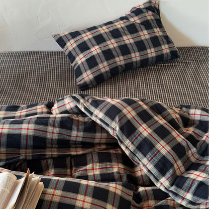 Detail view of the cotton muslin duvet cover set showing the contrast between the large dark plaid duvet and the small gingham-style fitted sheet.