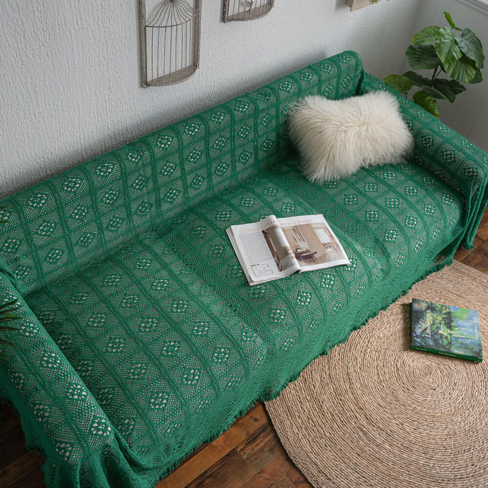 Green crochet lace sofa cover with tassel trim, fluffy cushion, magazine, and cozy home decor