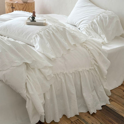 White cotton bedding set with ruffled trim on a bed in a cozy, rustic bedroom