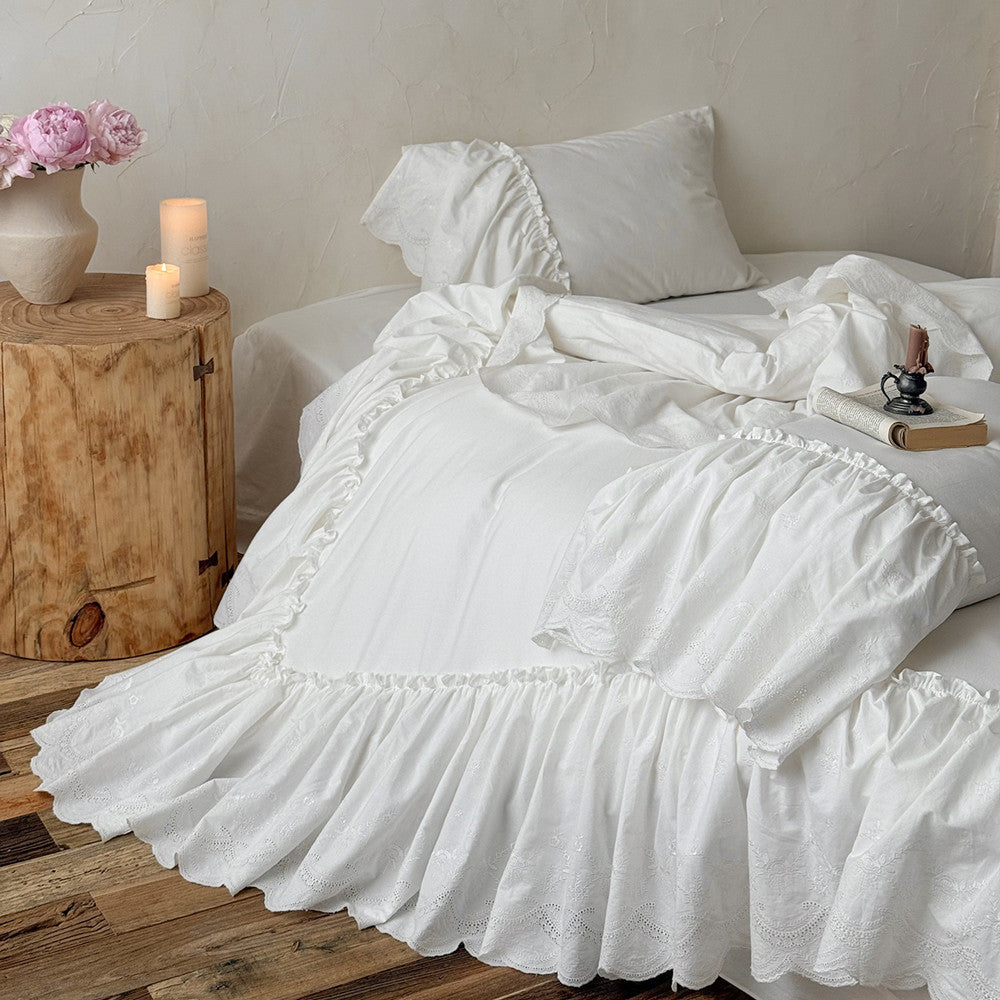 White cotton bedding set with ruffled trim on a bed, next to candles and pink flowers