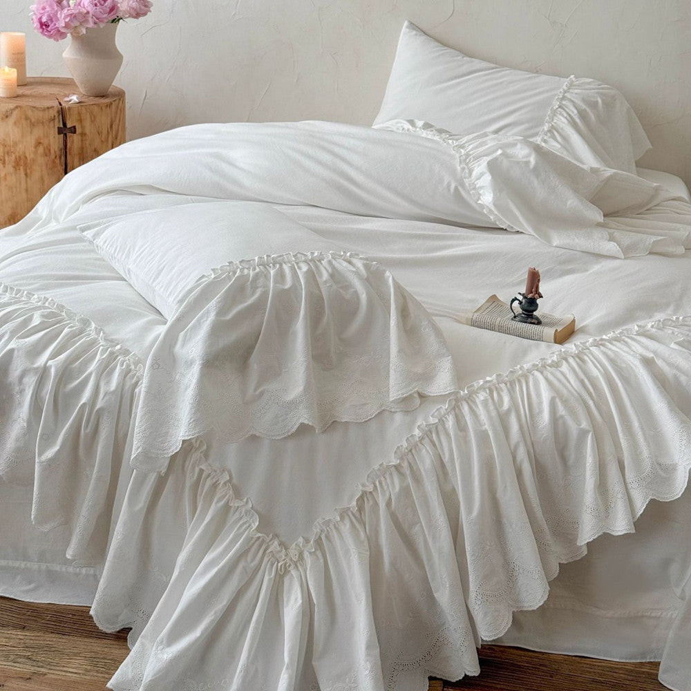 White cotton bedding set with ruffled trim on a bed in a cozy, softly lit bedroom
