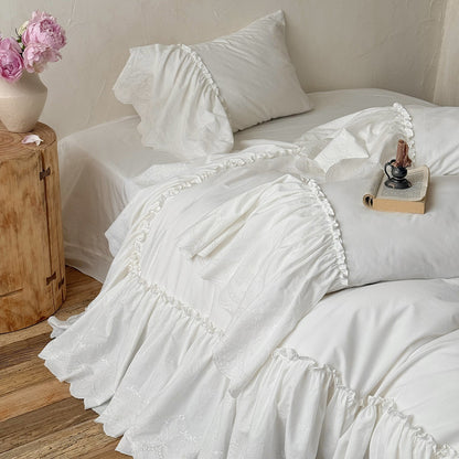 White cotton bedding set with ruffled trim in a cozy bedroom, floral vase on nightstand