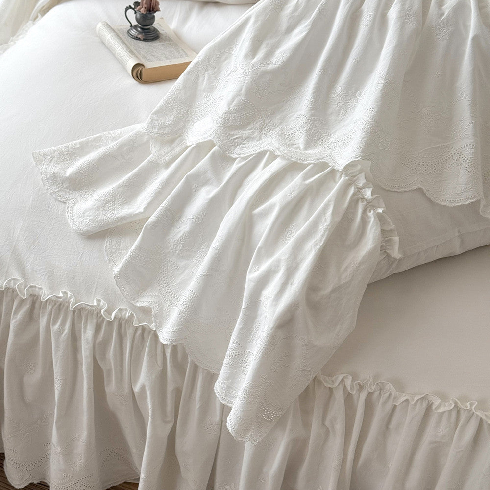 White cotton bedding set with ruffled trim and embroidered details on a bed