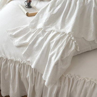 White cotton bedding set with ruffled trim and embroidered details on a bed