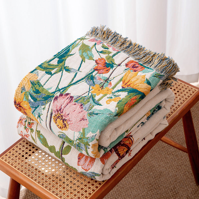 Folded wildflower garden cotton throw blanket with fringe on a rattan bench