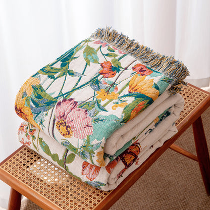 Folded wildflower garden cotton throw blanket with fringe on a rattan bench