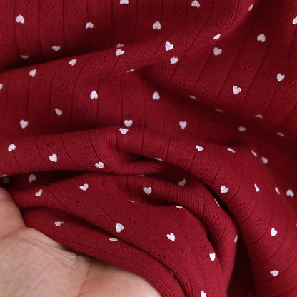 Red cotton pajama fabric with white heart print held in hand, soft and cozy texture