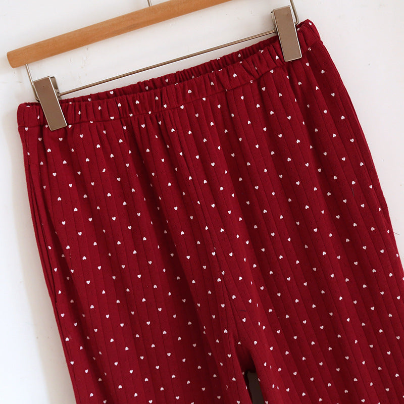 Red cotton pajama pants with white heart print and elastic waistband hanging on hanger