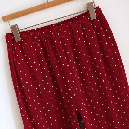 Red cotton pajama pants with white heart print and elastic waistband hanging on hanger