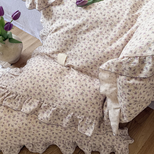 Floral patterned duvet cover with ruffles on a bed, accompanied by a vase of purple tulips.