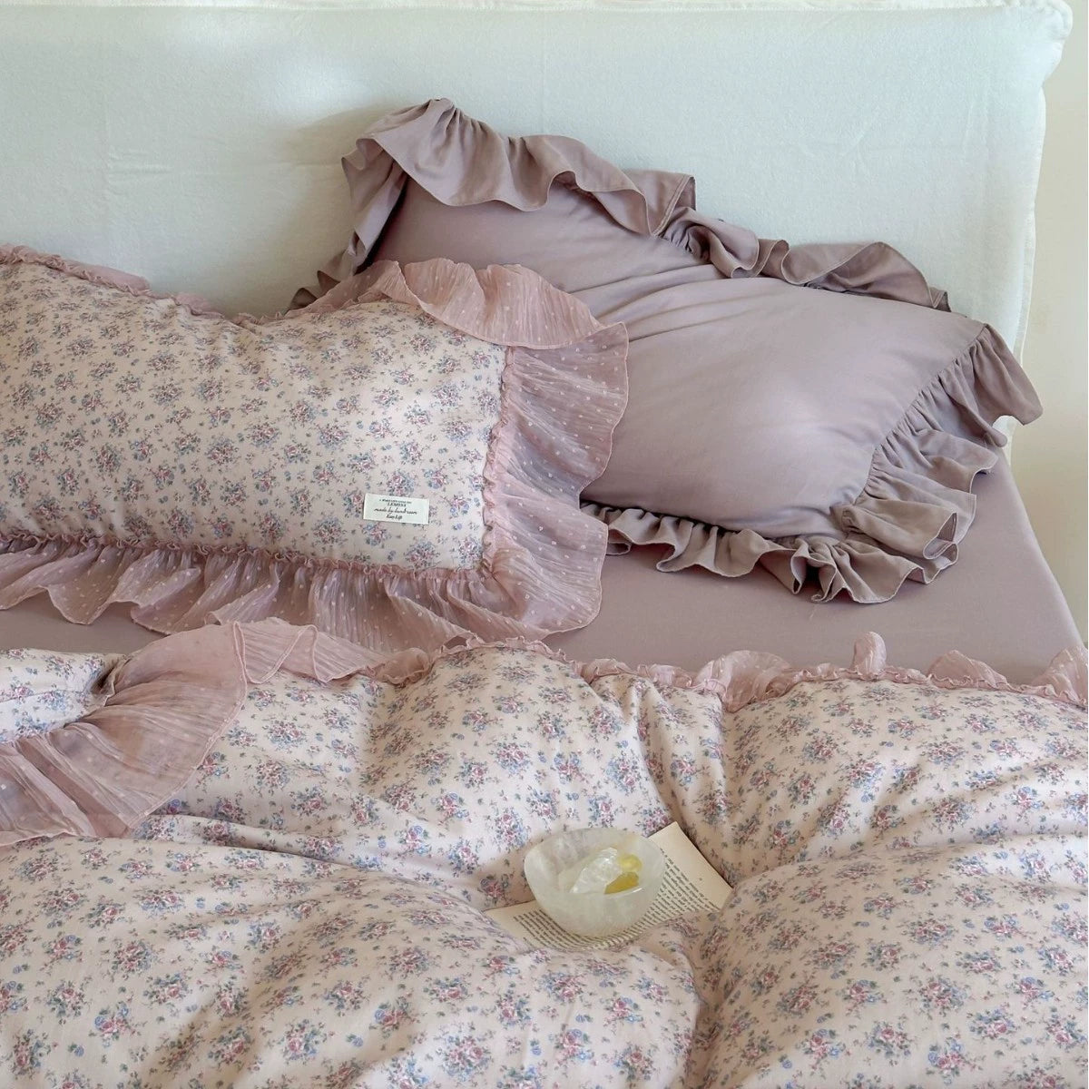 Close-up of the mixed floral and solid ruffled pillows: A floral ruffled pillow and a solid lavender ruffled pillow are placed side-by-side, emphasizing the mix-and-match effect of the different bedding elements.