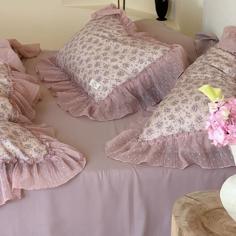 Close-up arrangement of multiple lavender floral ruffled pillows: Several floral pillow shams are neatly arranged on a solid lavender sheet, highlighting the soft ruffles and the texture of the dotted sheer fabric.