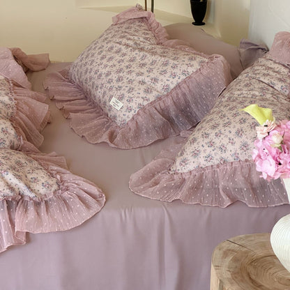 Close-up arrangement of multiple lavender floral ruffled pillows: Several floral pillow shams are neatly arranged on a solid lavender sheet, highlighting the soft ruffles and the texture of the dotted sheer fabric.