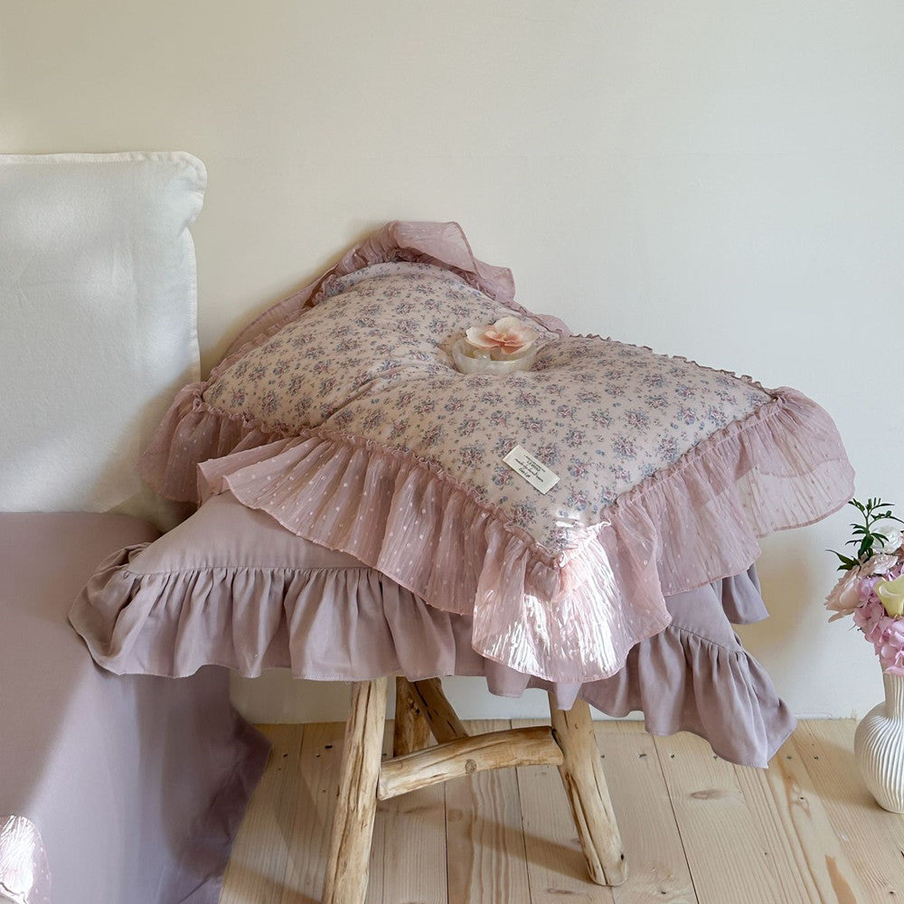 Stacked lavender ruffled bedding on a wooden stool: Floral and solid ruffled pillows and a coverlet are stacked on a rustic wooden stool, showcasing the home decor details.