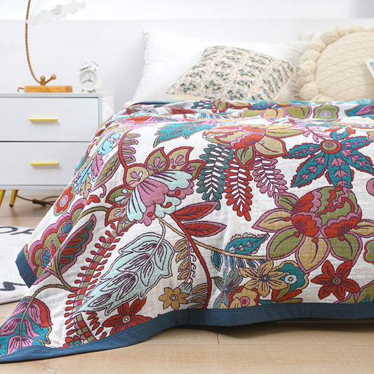 Close-up of a colorful retro floral cotton blanket on a bed with white and patterned pillows in a modern, bright bedroom