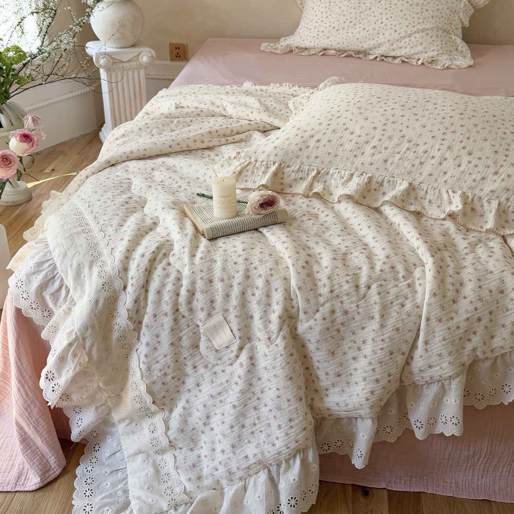 Close-up view of the ruffled lace comforter set featuring a ditsy floral print and wide eyelet lace borders, styled with a vintage book and candle for a romantic cottagecore look.