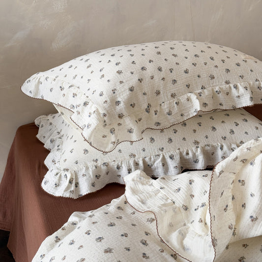 Stacked pillows from the Wild Pansy duvet cover set, showcasing the soft cotton muslin texture, delicate floral pattern, and the ruffled trim with brown stitching.