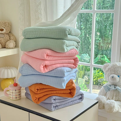 A stack of five folded 6-layer cotton gauze blankets in various colors: sage green, pink, sky blue, Terracotta, and grey.