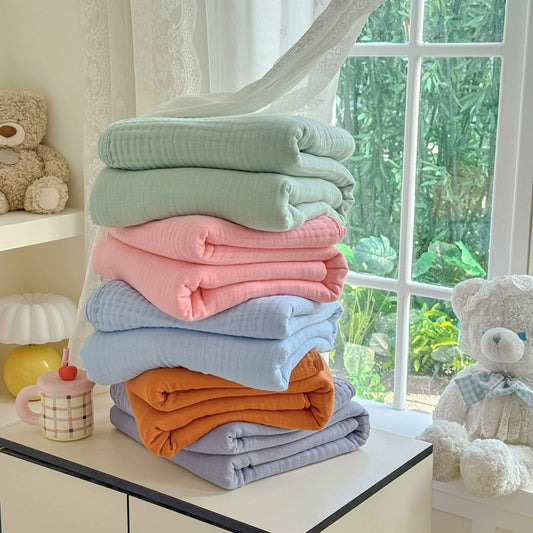 A stack of five folded 6-layer cotton gauze blankets in various colors: sage green, pink, sky blue, Terracotta, and grey.