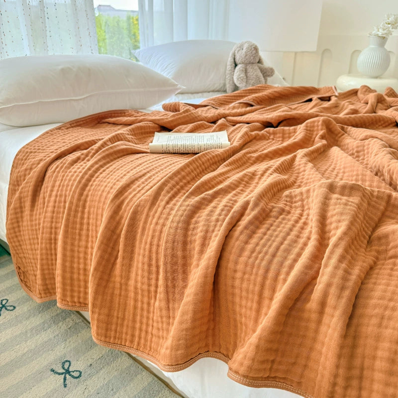 Burnt orange 6-layer cotton gauze blanket on a bed, showcasing the cozy, rumpled texture of the throw.
