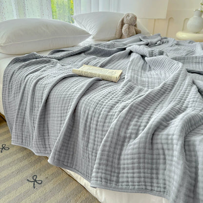 Light grey 6-layer cotton gauze blanket covering a bed, showing the cozy, pleated texture.