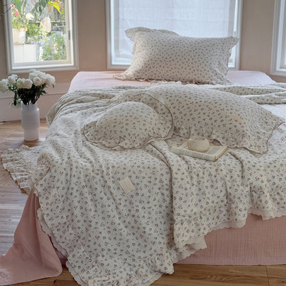 Lightweight cotton comforter with floral design and round ruffle pillow, styled in a cozy space